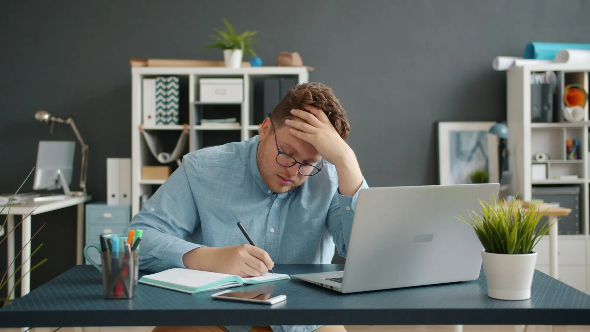 Stressed business owner writing at his desk in front of a laptop